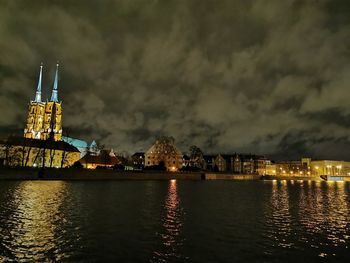 Illuminated buildings by river against sky at night