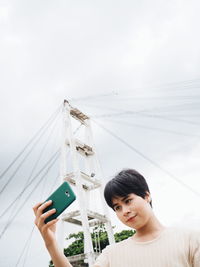 Young woman using mobile phone against sky