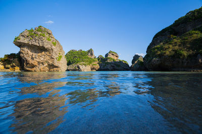 Rock formations in sea against clear blue sky