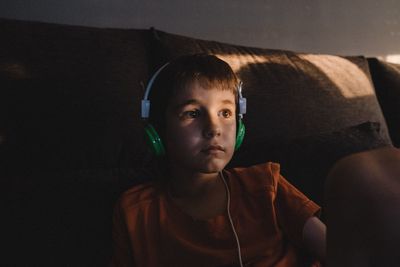 Boy wearing headphones while sitting on sofa