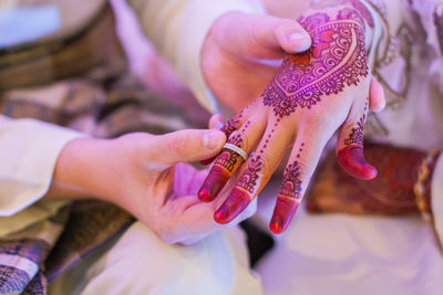 Midsection of groom putting ring in bride finger during wedding