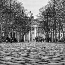 People walking on footpath by brandenburg gate against sky