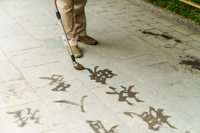 Low section of man writing with paintbrush while standing on footpath