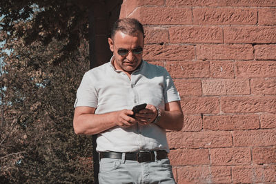 Man holding camera while standing against wall