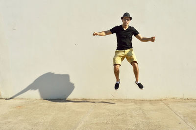 Full length of young man jumping on footpath against wall