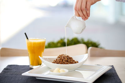 Cropped hand pouring milk on food by drink at restaurant