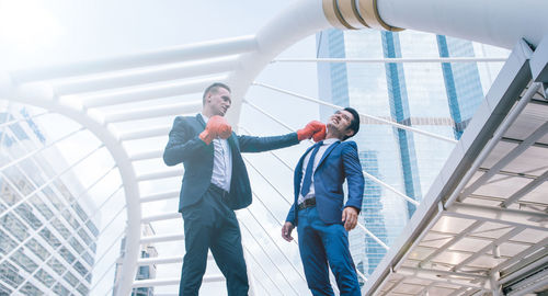 Low angle view of business colleagues with boxing gloves standing against buildings in city