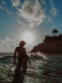 Rear view of woman standing on shore during sunset