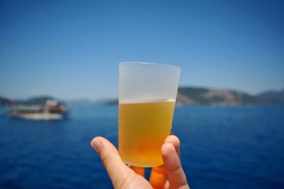 Close-up of hand holding drink against blue sky