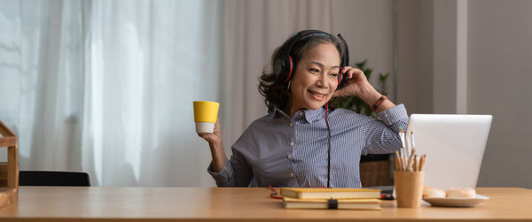 Smiling woman with headphones watching digital tablet at home