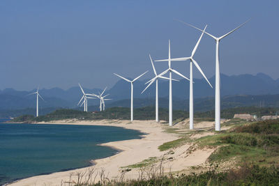 Wind turbines on land by sea against sky