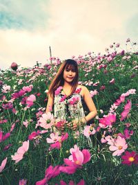 Portrait of beautiful woman with pink flowers on field against sky
