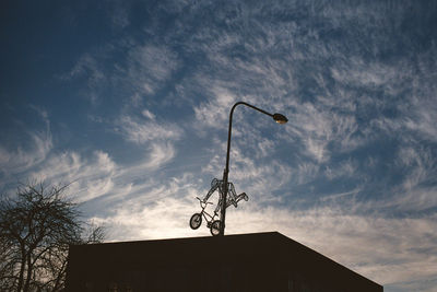 Low angle view of silhouette crane by building against sky