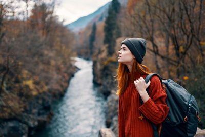 Woman looking away while standing on tree during autumn