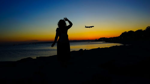 Silhouette person standing by sea against sky during sunset