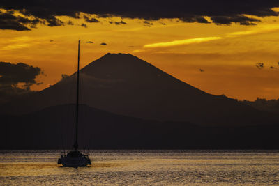 Silhouette sailboats in sea against orange sky