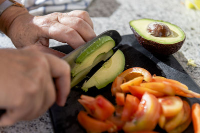 Close up of old lady hands chopping avocados and tomatoes.