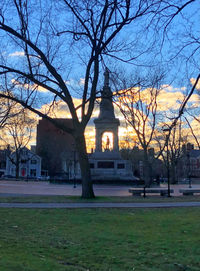 Bare trees and buildings against sky at dusk