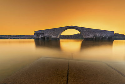 Arch bridge over river against orange sky