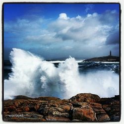 Waves breaking on rocks against cloudy sky