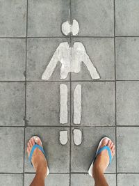 Low section of person wearing flip flop while standing on footpath with human representation