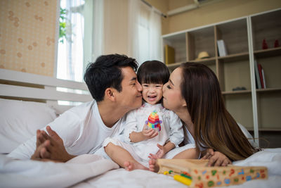 Parents kissing daughter on cheek at home