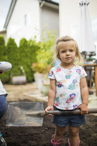 Portrait of cute blonde two-year-old helping dad with shoveling dirt.