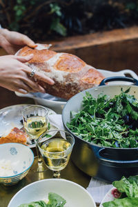 Woman breaking bread at summer evening dinner table with salad, white wine, steamed mussels