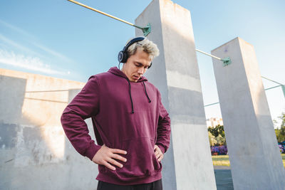 Young man looking away while standing against sky