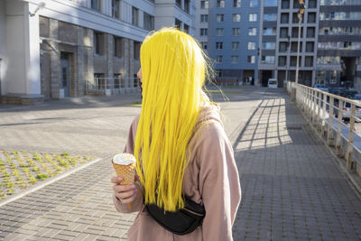 Young woman looking away while eating ice cream cone standing on street