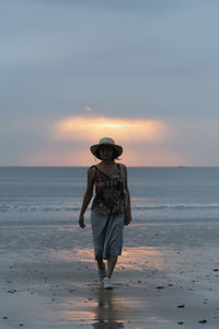 Full length of woman standing on beach against sky during sunset