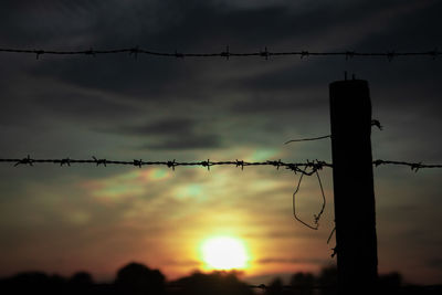 Close-up of silhouette barbed wire fence against sky during sunset