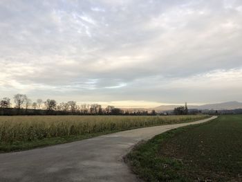 Empty road amidst field against sky