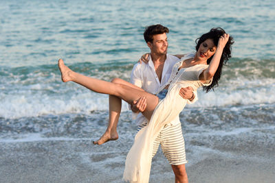 Boyfriend carrying girlfriend while standing at beach