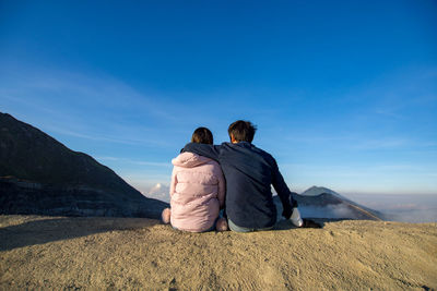 Rear view of couple sitting on mountain against sky