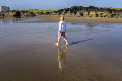 A blond woman walking alone and barefoot in the surf on a sunny day at rhosneigr beach, anglesey, uk