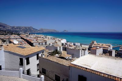 High angle view of townscape by sea against clear blue sky