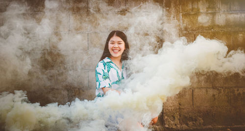 Portrait of smiling young woman amidst smoke against wall