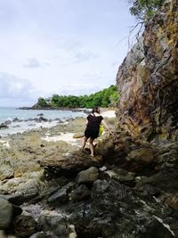 Full length of man on rock at beach against sky