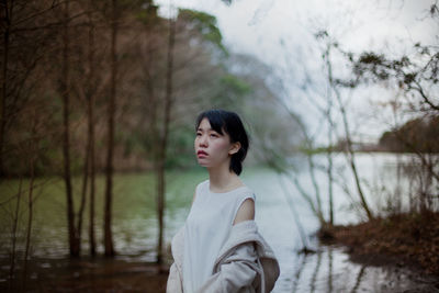 Young woman standing by lake against trees