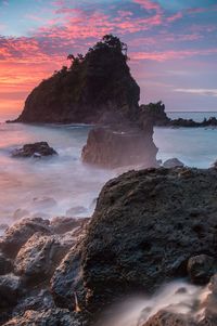 Rock formation on beach against sky during sunset