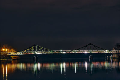 Illuminated bridge over river against sky at night