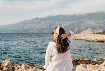 Rear view of young woman in white shirt standing on beach. sea, summer, view, lifestyle.