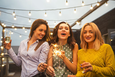 Happy female friends with drinks standing in yard