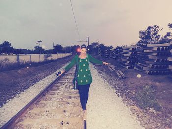 Portrait of young woman standing by trees against sky