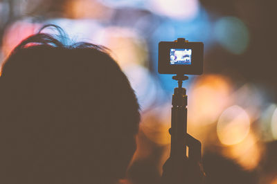 Rear view of silhouette man holding tripod with camera at night