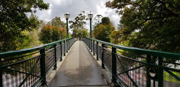 Footbridge in forest against sky