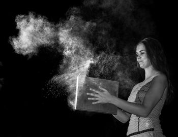 Young woman holding book while standing amidst powder against black background