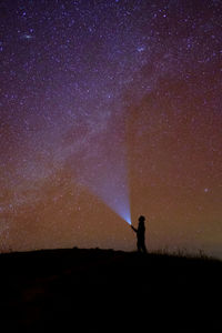 Lone hiker pointing flash light towards the milky way and andromeda galaxy in the night.