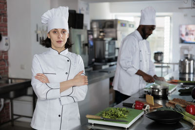 Female chef with arms crossed standing in kitchen